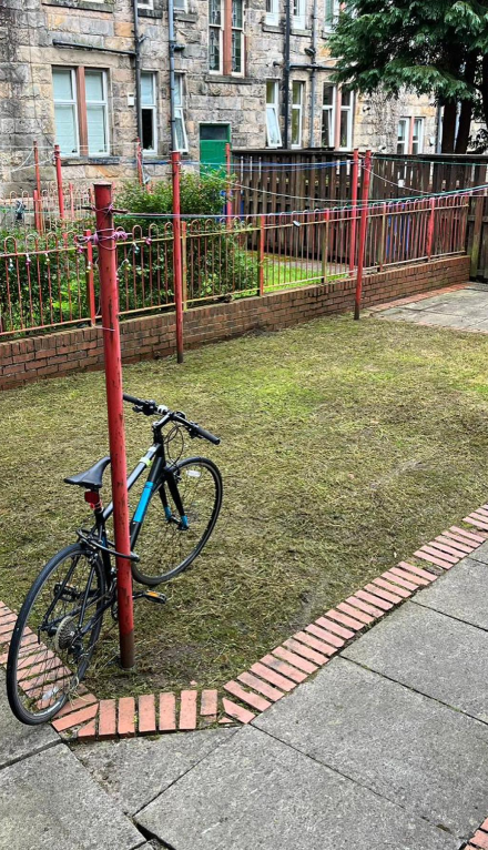 A older ruined small grass area that still has been very well cut in the back of a communal building with a bicycle in the corner