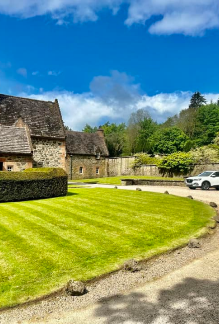 A beautiful stately home front garden with superbly mowed grass and pebble stones around the large front parking area with a 4 by 4 vehicle parked at the corner